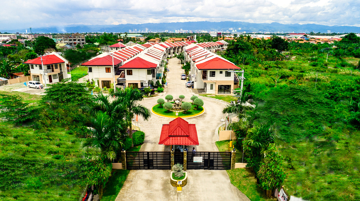 Elevated view along a landscaped avenue of red-roofed houses at Anami Homes Mactan, with a planted island at its centre